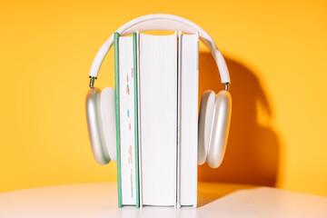 White wireless headphones on a stack of books in front of a yellow background.