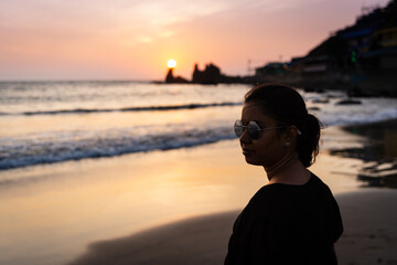Fototapeta premium Beautiful young Indian woman Enjoying the beautiful sunset at Goa Beach in India. Delightful girl enjoying Sunset at beach - Healthy lifestyle concept with female smiling.