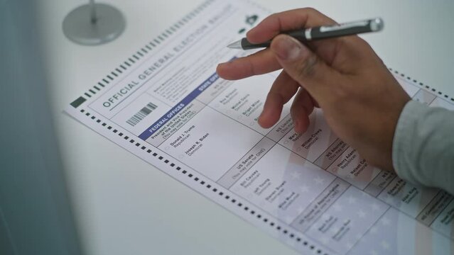 Close up of anonymous African American man choosing which presidential candidate to vote for in paper ballot in voting booth. US citizen at polling station. National Elections Day in United States.