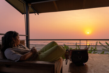 Mature young Indian woman enjoying sunset at Goa sea beach while sitting in a comfortable couch