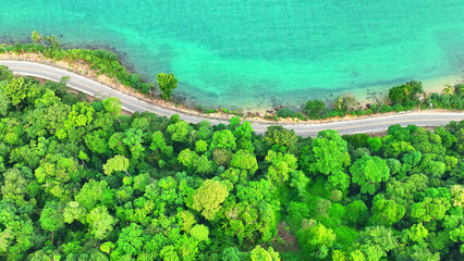 An epic drone shot captures a tropical coastal road, flanked by vibrant greenery and crystal-clear...