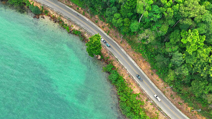 Aerial spectacle of cars navigating a coastal paradise, where azure waters meet a lush shoreline, creating an unforgettable driving experience. Ko Chang island, Thailand. 
