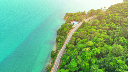 A stunning bird's-eye perspective of a coastal asphalt road, nestled between lush greens and...