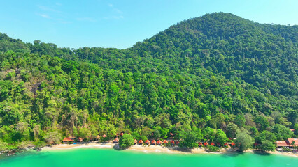 Turquoise waters kiss golden shores, while resorts line the beach. Towering mountains covered in...