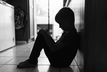 Sad little boy alone on floor in a dark room	