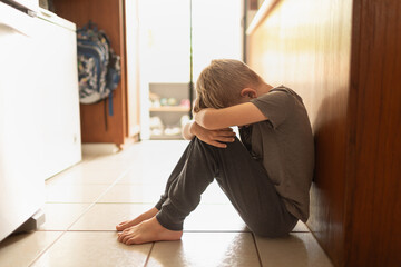 Sad upset little boy head down sitting on the floor at home 	 - obrazy, fototapety, plakaty