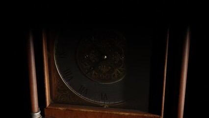 Close-up of the dial of an antique grandfather clock in a dark room, illuminated by light from the window.