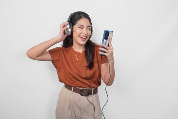 Happy young Asian woman in brown shirt smiling and listening to music from smartphone using wireless headphone.