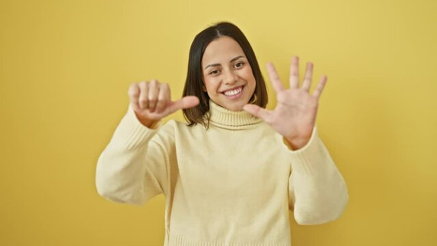Radiant hispanic young woman standing in yellow isolated background, gleefully pointing up with fingers, confidently showing number six - strutting a sweater with a charming smile.