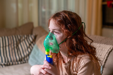 Sick girl making inhalation with nebulizer to reduce coughing, lying in bed at home, child taking...