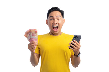 Excited young Asian man holding smartphone and money, looking at camera with surprised expression isolated on white background