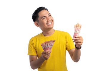 Happy young Asian man holding bunch of money and looking up isolated on white background