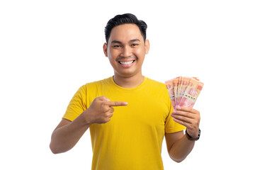 Happy young Asian man pointing finger at money in his hand isolated on white background. Profit and wealth concept