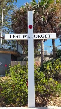 lest we forget, white memorial cross with words and single red poppy flower outdoors in Australia