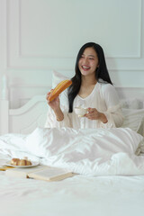 Attractive beautiful woman eats breakfast and healthy fruit drink in bed while happy and smiling alone in the morning. Lifestyle concept, working holidays.