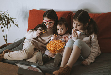 Three girls are watching a movie sitting on the couch.