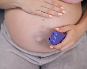 A pregnant woman smokes a vape while sitting on the couch. Close-up of the belly with allergies.