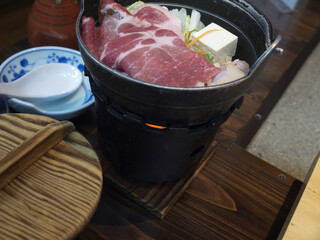 Cooking japanese Sukiyaki soup of pork meat and tofu in iron pot on fire for traditional ryokan dinner