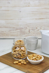 Kacang goreng or fried peanuts in a jar and white plate. Indonesian snack with marble white background, selective focus.