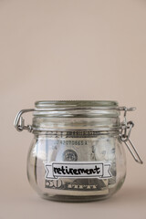 Saving Money In Glass Jar filled with Dollars banknotes. RETIREMENT transcription in front of jar....