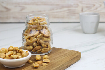 Kacang goreng or fried peanuts in a jar and white plate. Indonesian snack with marble white background, selective focus.