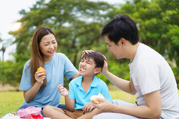 Happy cheerful Asian family with father, mother, and little son enjoy picnic together in a weekend...