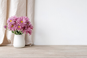 Empty beige wooden table and white concrete wall surface, vase with pink flowers bouquet, linen curtain background. Podium backdrop template for product placement, blank copy space