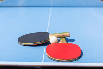 Red and black Table Tennis Paddles and ball on the blue table tennis table with net. Ping Pong concept with copy space