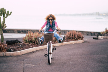 Naklejka premium One young lady riding bike alone on the street with ocean coastline view. Outdoor leisure activity green transport woman. People and healthy lifestyle. Concept of tourist on vacation having fun