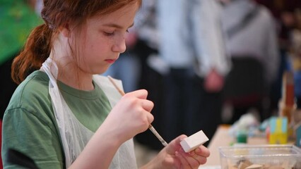 girl makes a wooden product with her own hands, paints it with white paint, exhibition of crafts, crafts fair, education, master classes, DIY wood product