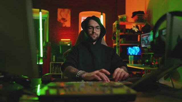 Hacker writing code cracking computer. Man programmer in hoodie cracks system, using computer in dark room. Hacker attack, technology, virus infected software, anonymous, cyber security concept.