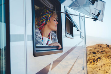 Camper in a desert setting with a curly-haired woman with a scarf on her head leaning against the...