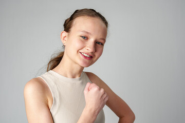 Young Woman in Casual Attire Smiling and Making a Fist Pump Gesture on a Plain Background