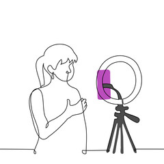 Woman broadcasts while standing in front of a phone camera mounted on a ring lamp - one line art vector. concept live stream of a female blogger