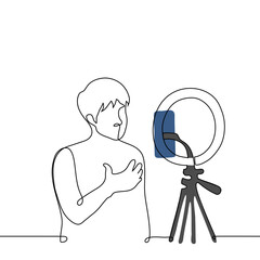 man broadcasts while standing in front of a phone camera mounted on a ring lamp - one line art vector. concept live stream of a male blogger