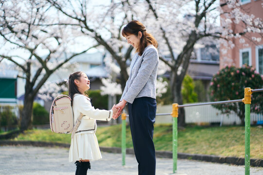 桜の咲く公園で手を繋いで見つめ合う日本の母と娘