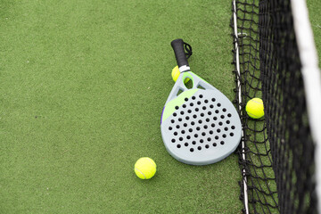 Closeup view of a paddle racket and balls in a padel tennis court near the net. Green background with white lines. Sport, health, youth and leisure concept. Sporty equipment. 