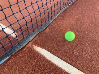 the bright green tennis ball lands on the clay court close to the opponent's net