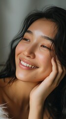 Naklejka premium Close-up portrait of a cheerful young Asian woman with her hand on her face, showcasing natural beauty