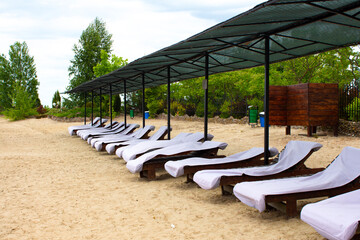 Beach recreation area on the shore of the lake. Empty deck chairs are standing on the sand.