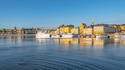 Boats anchored in the calm waters of Stockholm Harbor under a clear blue sky, with the city...