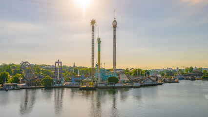 The sun rises on Grona Lund, Stockholms waterfront amusement park, casting a warm glow over the thrill rides and serene waters.
