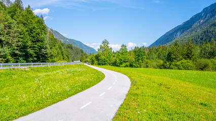 A winding bicycle path cuts through the lush greenery of the Upper Sava Valley with picturesque mountain views under a clear blue sky. Julian Alps, Slovenia