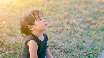 Cute Asian toddler sitting relaxed on the grassy field.