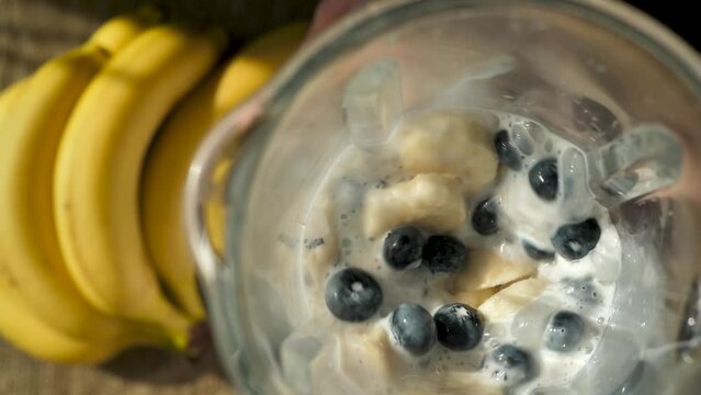 The process of preparing a banana smoothie with milk and blueberries in a blender. top view chopping and mixing fresh berries and fruits with milk in a blender glass. Make your own nutritional shake