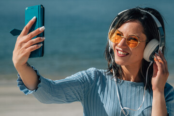 woman with headphones and mobile phone listening to music on the beach