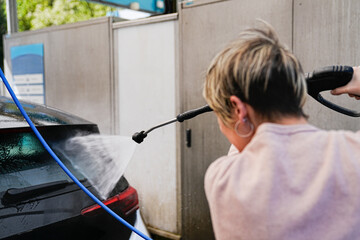 A woman in action, washing her car with a dynamic water jet.