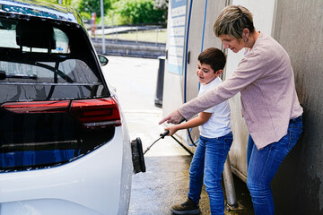 Son aids his mother in car washing, focusing on the rear end.