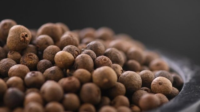 Allspice (Jamaica pepper, Pimento) spice heap rotating over black background. Whole Black peppercorns close up. Slow motion.