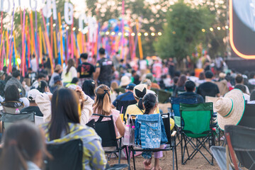 Crowd of people are sitting in chairs at a concert. Scene is lively and energetic, Summer festival concert. - obrazy, fototapety, plakaty